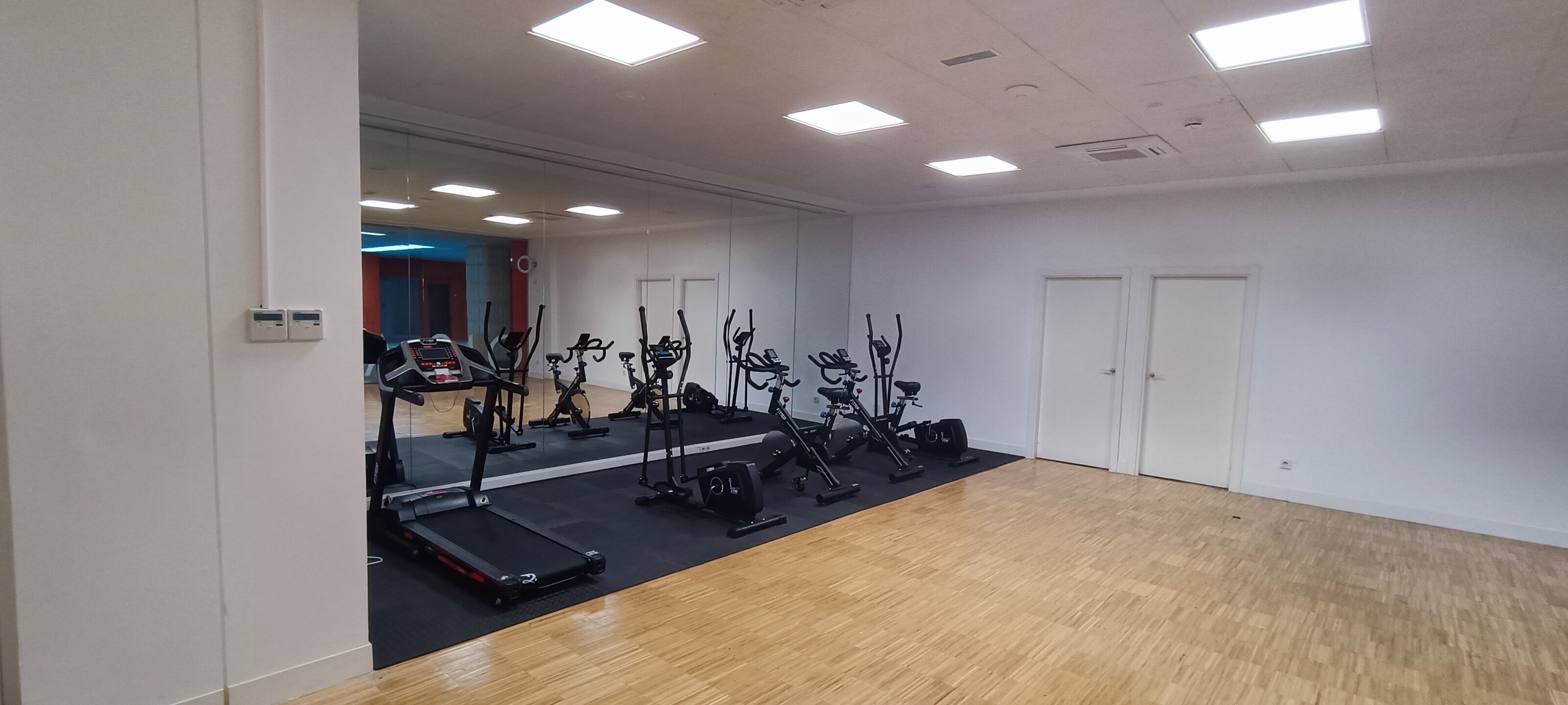 Un gimnasio con equipo de ejercicio, un espejo y suelo de madera.