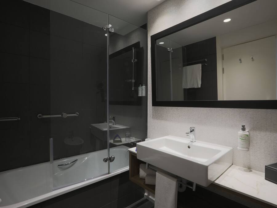 Un baño moderno con cabina de ducha de vidrio, un lavabo blanco y un espejo grande.