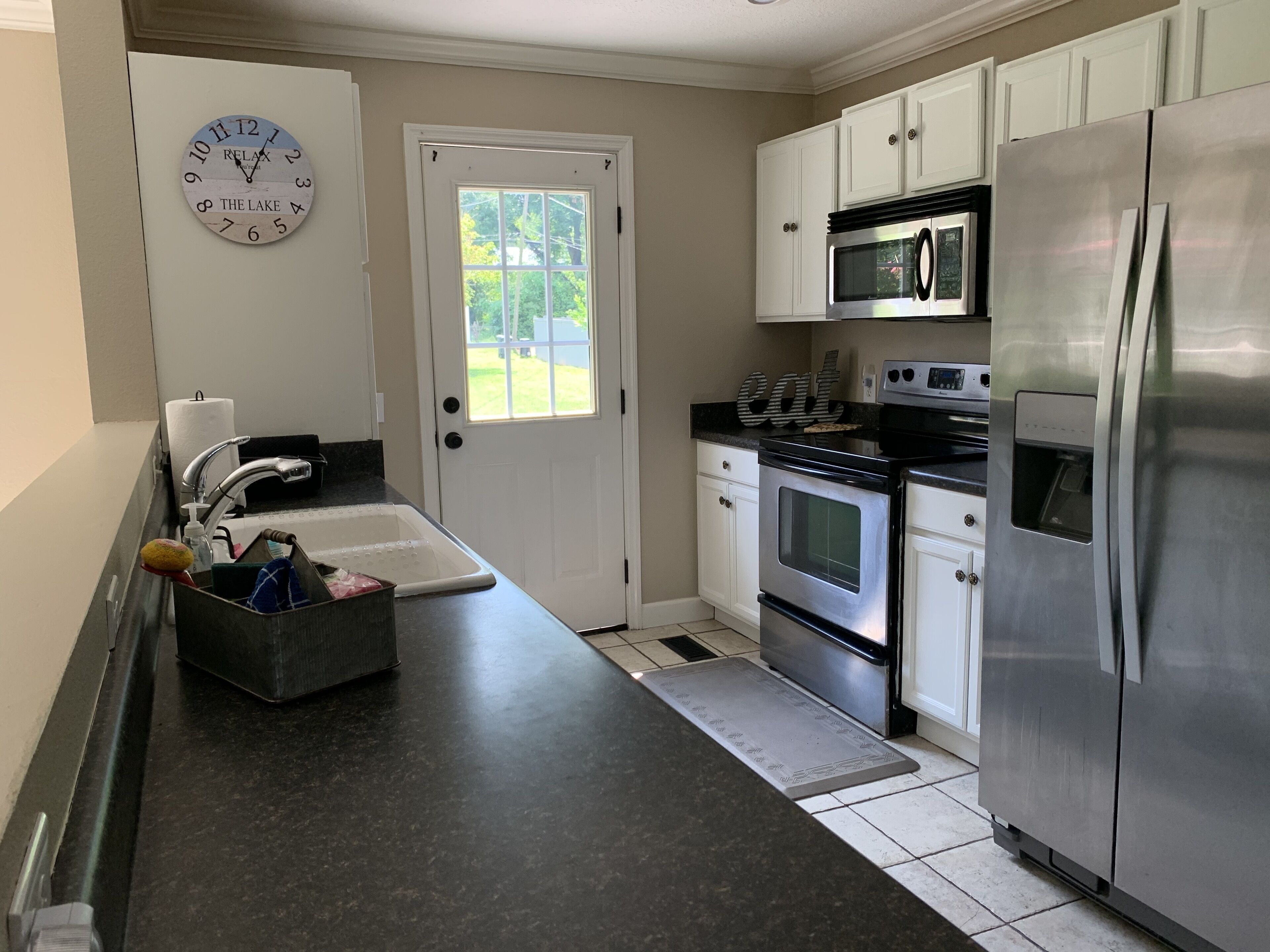 A kitchen with white cabinets, a stainless steel refrigerator, a built-in oven, a microwave, and a sink with a soap dispenser.