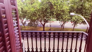 A balcony with a wrought iron railing overlooking a street lined with trees and a parked car. - Casa de huéspedes asturiana (Madrid)