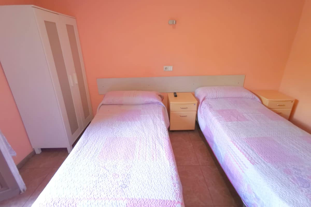 A room with two single beds, a wardrobe, and a nightstand with a lamp.