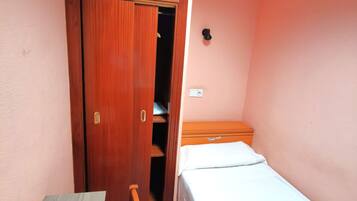 Un dormitorio pequeño con un armario de madera, una cama individual y una mesita.