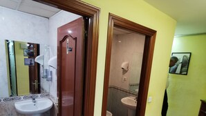 A bathroom with a sink, toilet, and shower. There is a yellow trash bin and a mirror. The walls are yellow, and the floor has patterned tiles. - Casa de huéspedes asturiana (Madrid)