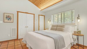 A bedroom with a bed, a window with blinds, a bedside table, and a wall-mounted light fixture. - Rosemary Cabin I Couples, Stargazing, Hill Country (Wimberley)