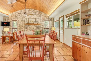 A dining area with a stone wall, wooden ceiling, and a television mounted on the wall.