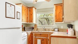 A kitchen with wooden cabinets, a white refrigerator, a stove, a sink, and a window with a view of trees. - Rosemary Cabin I Couples, Stargazing, Hill Country (Wimberley)