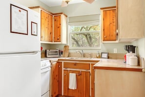 Une cuisine avec des meubles en bois, un réfrigérateur blanc, une cuisinière, un évier et une fenêtre donnant sur des arbres.