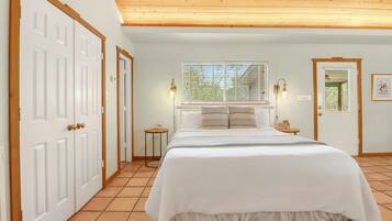 A bedroom with a bed, two bedside lamps, a window with blinds, and a door.