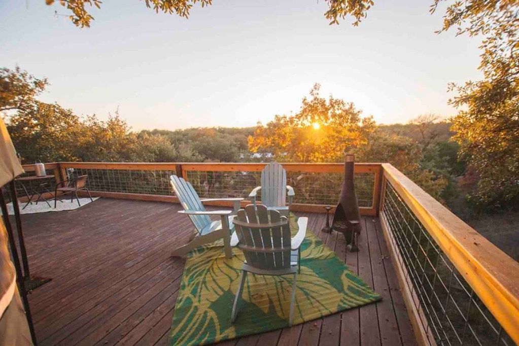 A wooden deck with outdoor seating and a view of trees and the sunset.