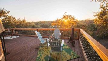 A wooden deck with outdoor seating and a view of trees and the sunset.
