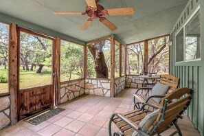 A covered patio with stone walls, wooden furniture, and a ceiling fan.
