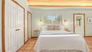 Een slaapkamer met een bed, twee bedlampen, een raam met zonwering en een deur.