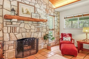 A stone fireplace with a metal screen, a red chair with a patterned cushion, and a window with blinds.