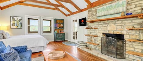 Una habitación acogedora con cama, sofá azul estampado, mesa de centro de madera, chimenea de piedra y vigas de madera en el techo.
