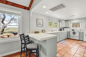 A kitchen with a large island, bar stools, a window with a view, and a tiled floor.