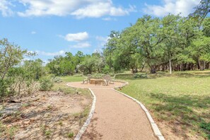 Un espacio de estar al aire libre con forma circular, que incluye una mesa y sillas de piedra, rodeado por un sendero de grava y follaje.