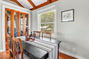 A dining area with a long table, wooden chairs, and a view of trees through a window. - Prickly Pear Cabin I Stargazing, Couples (Wimberley)