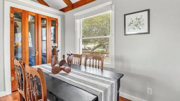 A dining area with a long table, wooden chairs, and a view of trees through a window.