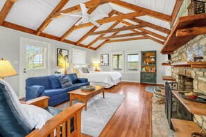 A cozy room with a wooden ceiling, a sofa, a bed, and a stone fireplace.