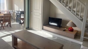 A living room with a TV, a wooden bench, a staircase, and a dining area with chairs and a table. - Beautifully furnished flats with sea view (Lecci)