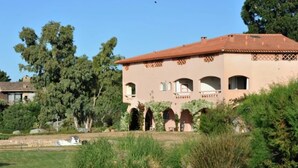 A large, single-story building with a red-tiled roof, surrounded by greenery and trees. - Beautifully furnished flats with sea view (Lecci)