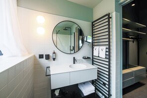 A modern bathroom with a white sink, a round mirror, and a towel rack. - Hôtel Vedette (Profondeville)