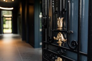 A black wrought iron gate with a golden decorative element, leading to a hallway with a light source at the end. - Hôtel Vedette (Profondeville)