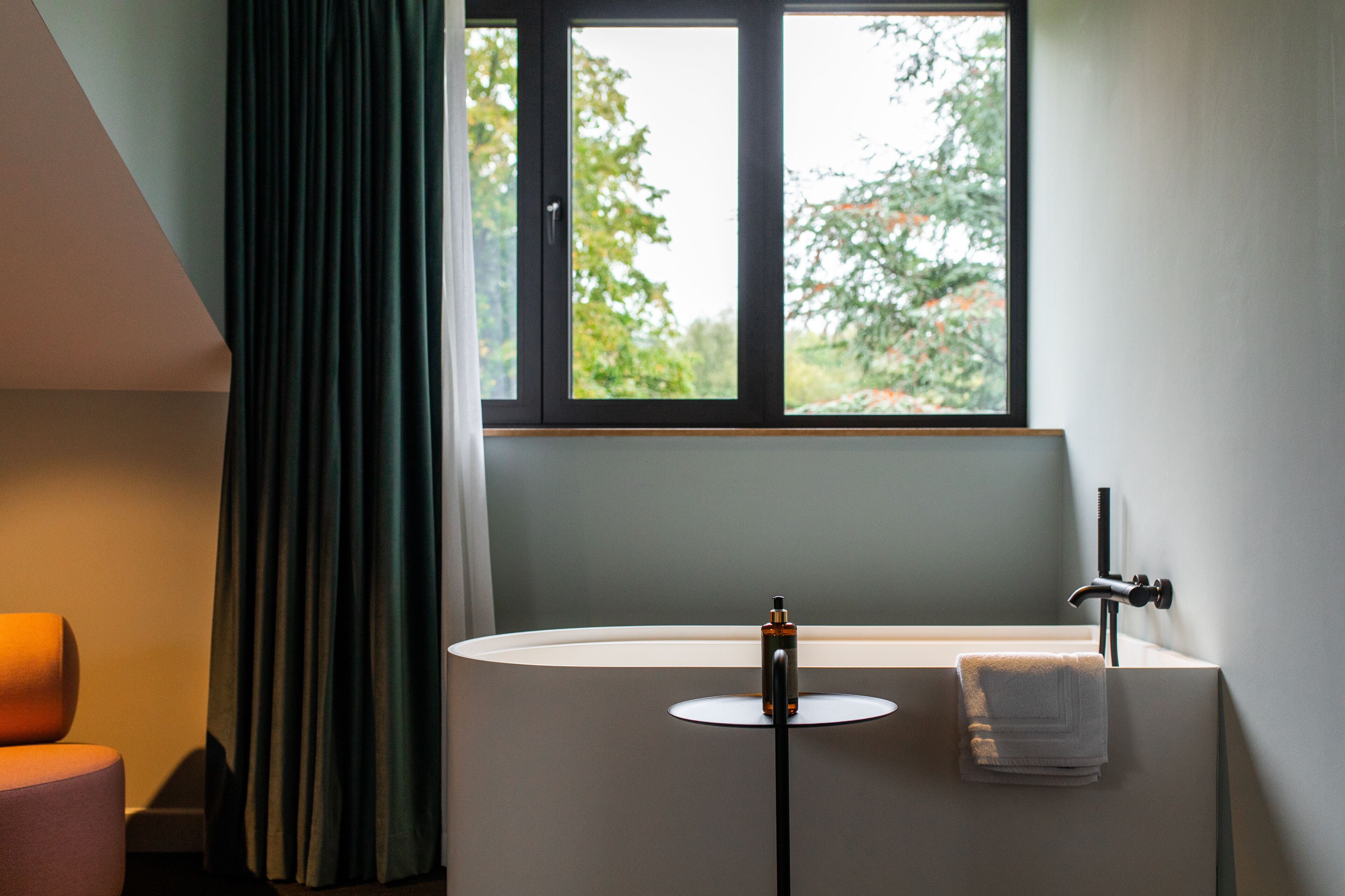 A modern bathroom with a freestanding bathtub, a towel, and a window with a view of trees.