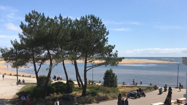 A beachside view with a parking area, picnic tables, and a few people walking. - Appartement Bord de mer (Guidel)