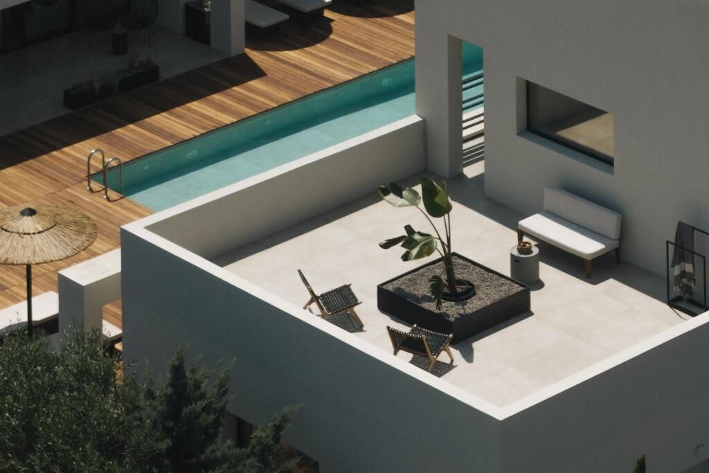 A rooftop pool area with a wooden deck, lounge chairs, a small table, and a potted plant.