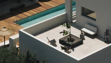 A rooftop pool area with a wooden deck, lounge chairs, a small table, and a potted plant.