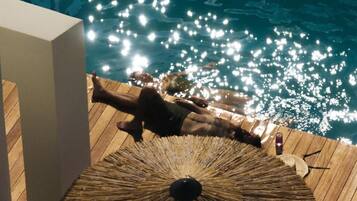 A person lying on a wooden deck by a pool with a straw umbrella.