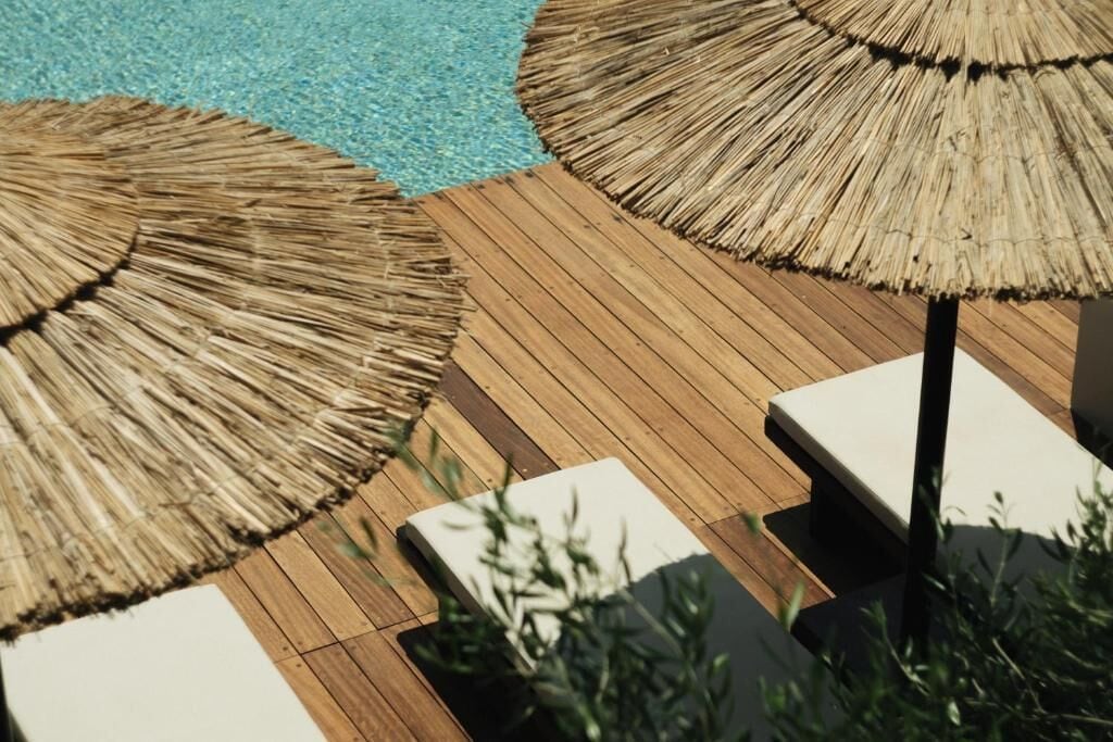Eine Holzterrasse mit Reetdachschirmen und weißen Liegestühlen.
