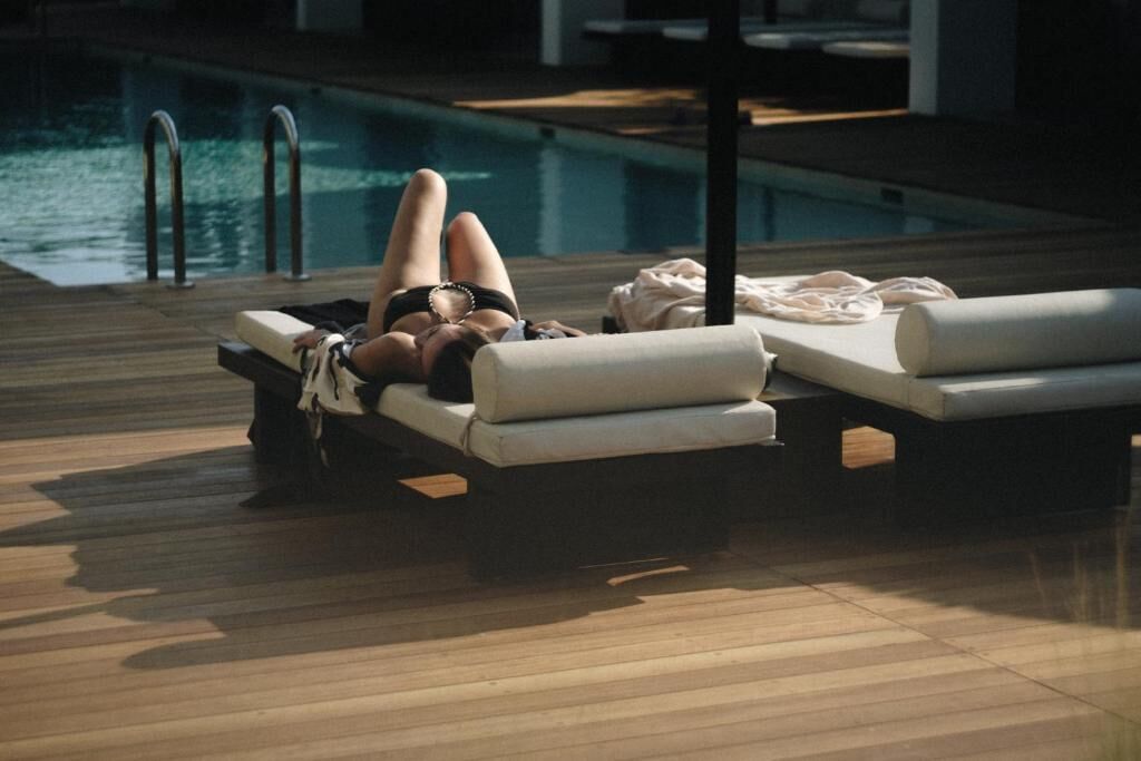A poolside lounge area with wooden flooring, lounge chairs, and a pool.