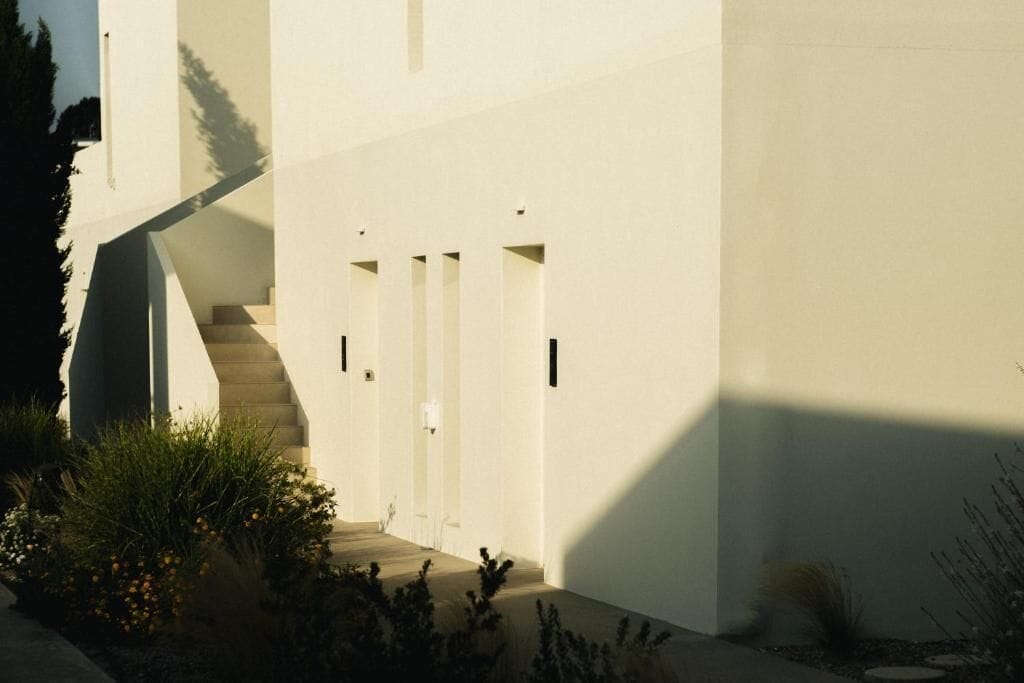 A modern building with a staircase leading to a door, surrounded by greenery.