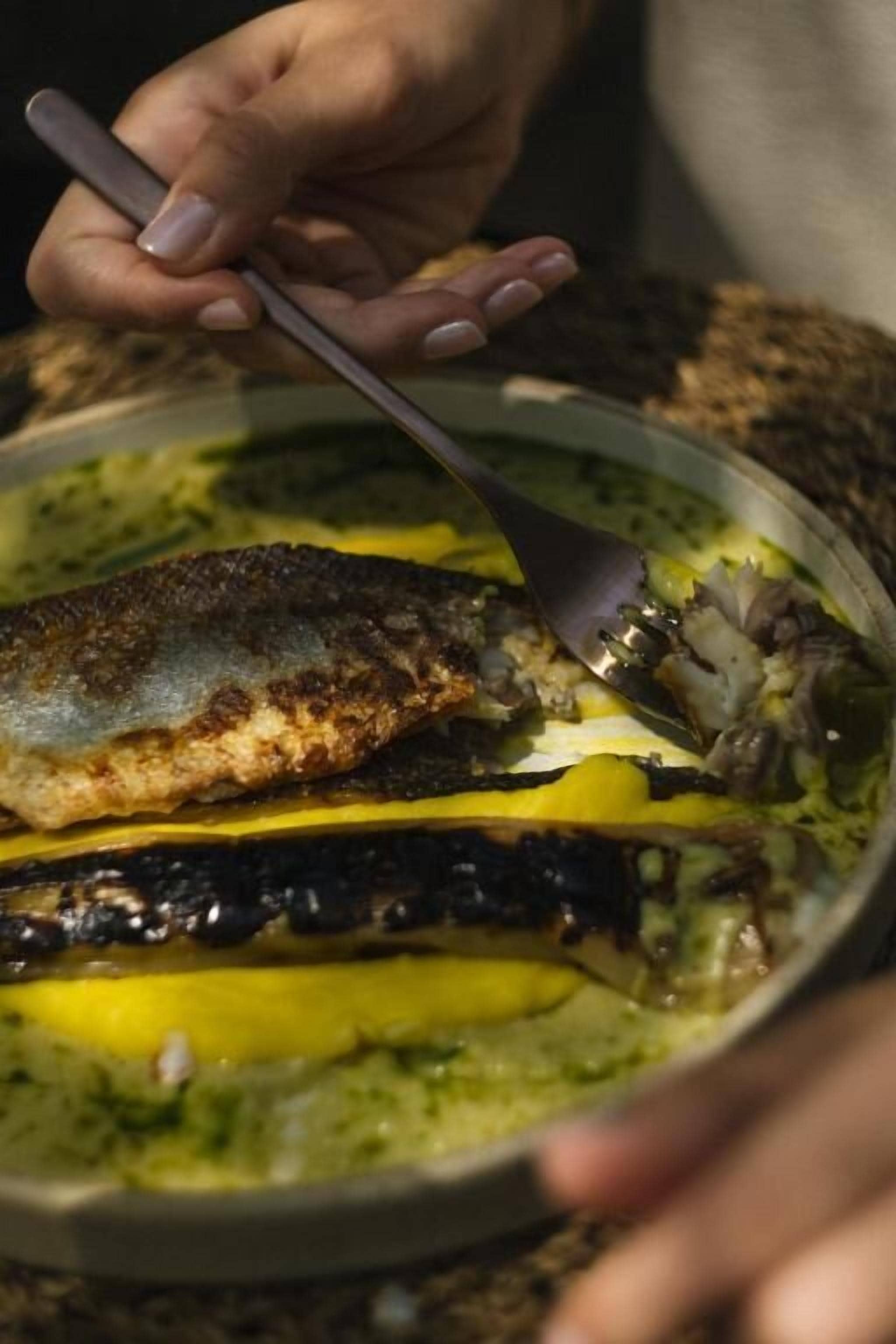 Una persona sirve un plato con pescado y verduras en un bol.
