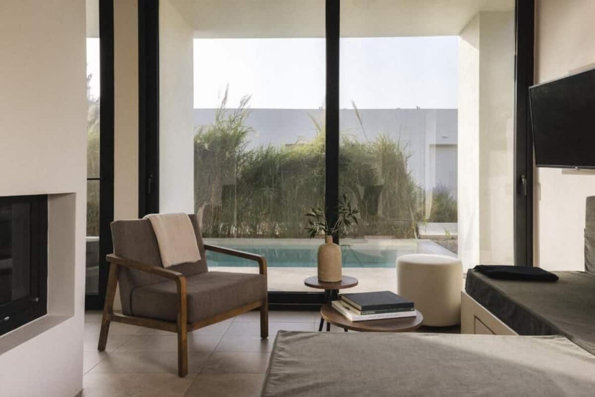 A modern living room with a large window, a pool view, a flat-screen TV, and a comfortable seating area.
