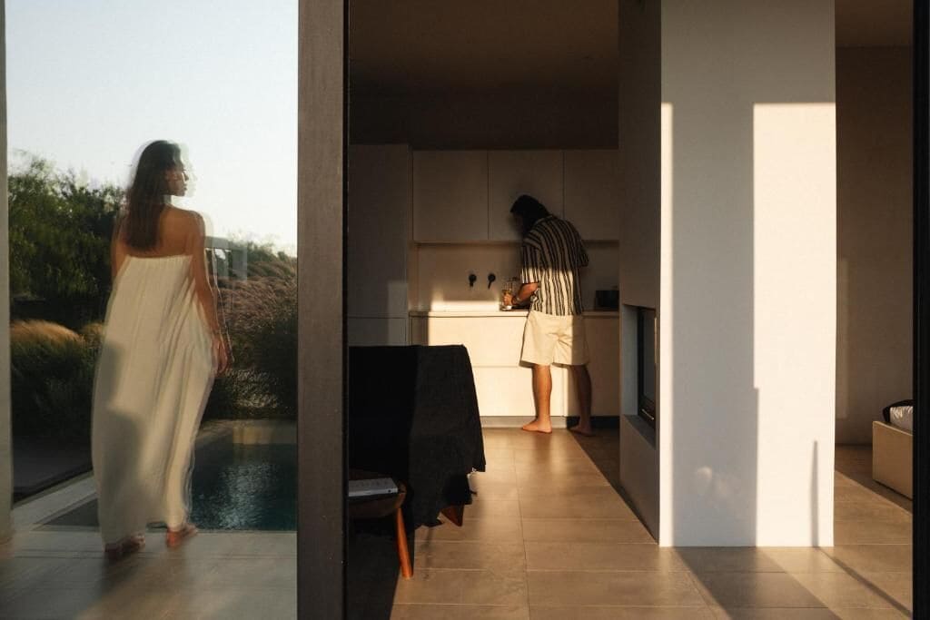 A modern kitchen with a person cooking, a dining area with a table and chairs, and a view of a pool outside.