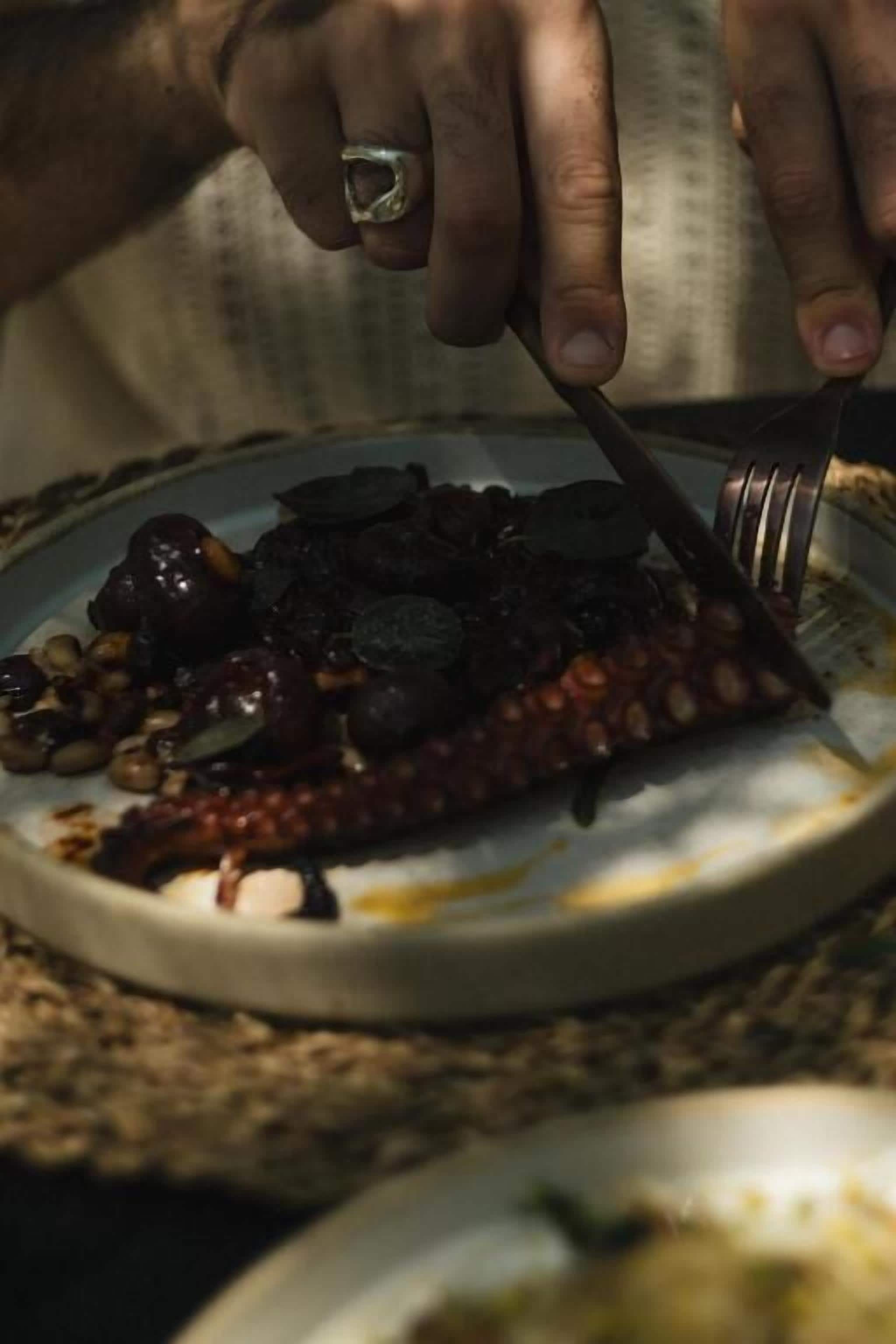 A hand holding a fork and knife, cutting into a plate of food.