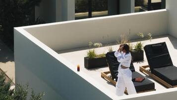 A rooftop terrace with lounge chairs, potted plants, and a person taking a photo.