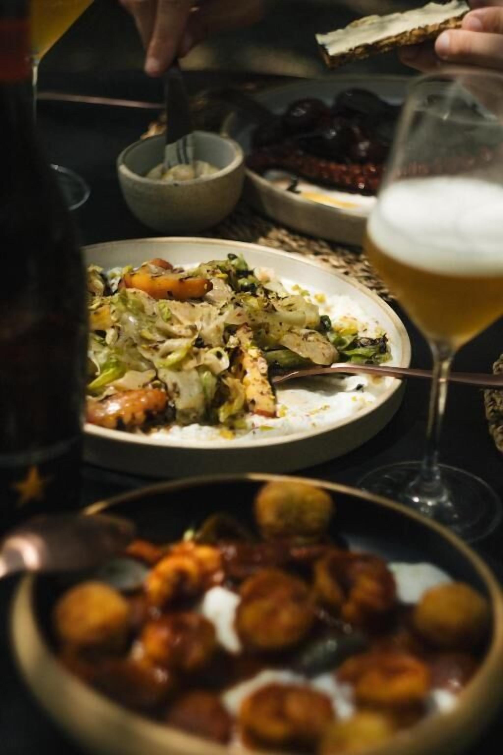 A dining table with a plate of food, a glass of beer, and a bowl of snacks.