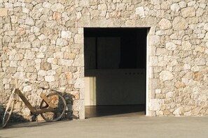 A stone wall with a doorway leading to a dark interior. A bicycle is leaning against the wall.