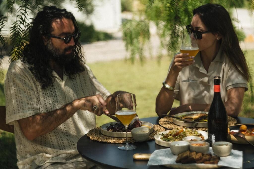 Two people dining outdoors at a round table with various dishes and drinks.