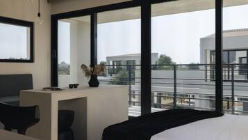 Un dormitorio moderno con una cama grande, un escritorio y vistas a edificios a través de amplios ventanales.
