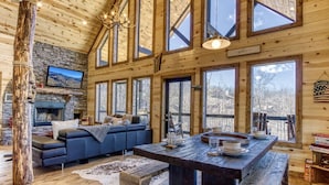 A rustic cabin interior with a stone fireplace, a large wooden dining table, and a cozy seating area.