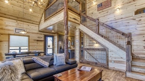 A log cabin interior with a wooden staircase, a black leather sofa, and a dining area.