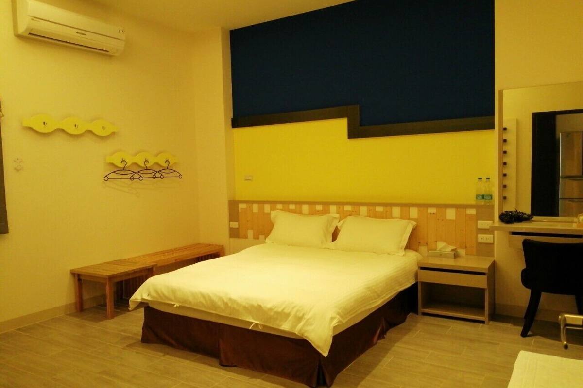 Quarto de hotel com cama, mesa de cabeceira, banco e espelho.