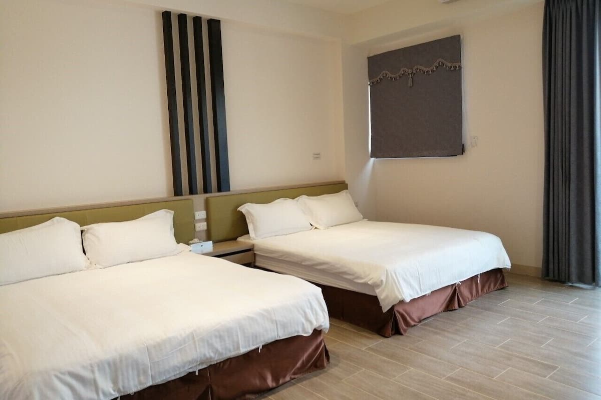 Quarto de hotel com duas camas, cabeceira, ar condicionado fixado na parede, janela com cortinas e um ornamento na parede.
