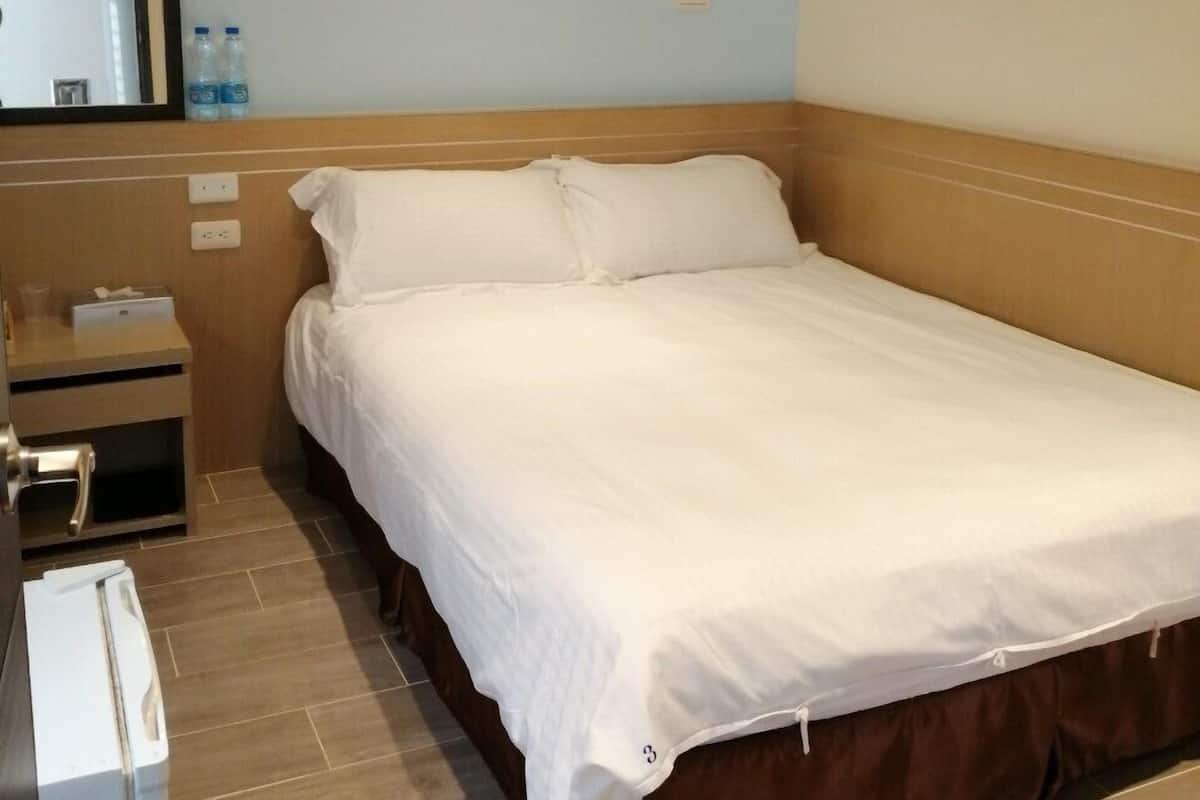Quarto de hotel com uma cama, mesa de cabeceira, espelho e uma tomada na parede.