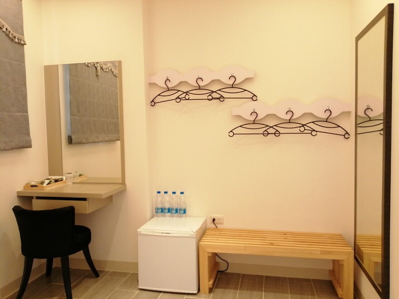 Een compacte badkamer met een wastafel, spiegel en een bankje. Op het bankje staan flessen en er is een kleine koelkast.